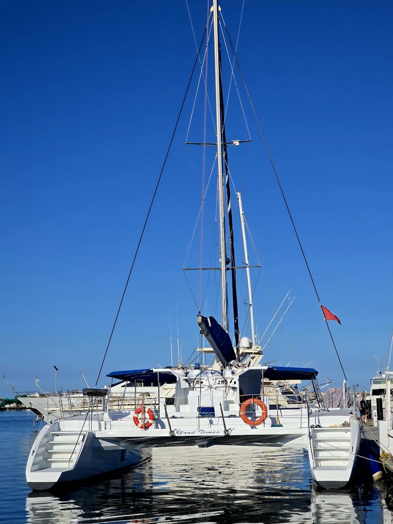 A sleek white catamaran docked at a marina, set against a brilliant blue sky.