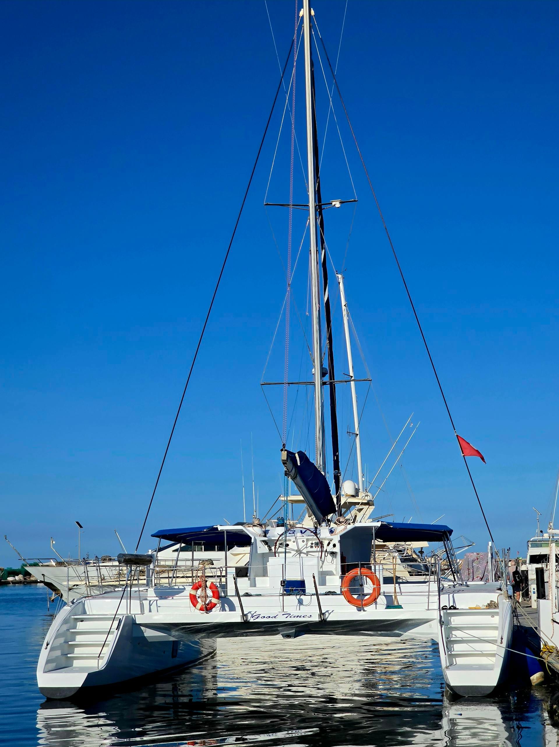 A sleek white catamaran docked at a marina, set against a brilliant blue sky.