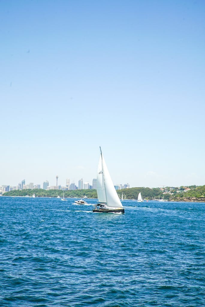 Sailboats cruising on the vibrant blue waters of Sydney Harbor with the city skyline in the background.