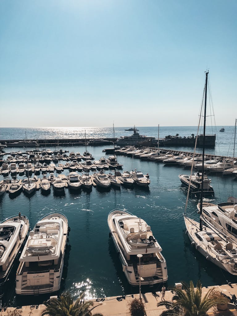 Scenic view of a marina with luxury yachts anchored in Monte Carlo, Monaco under a bright blue sky.