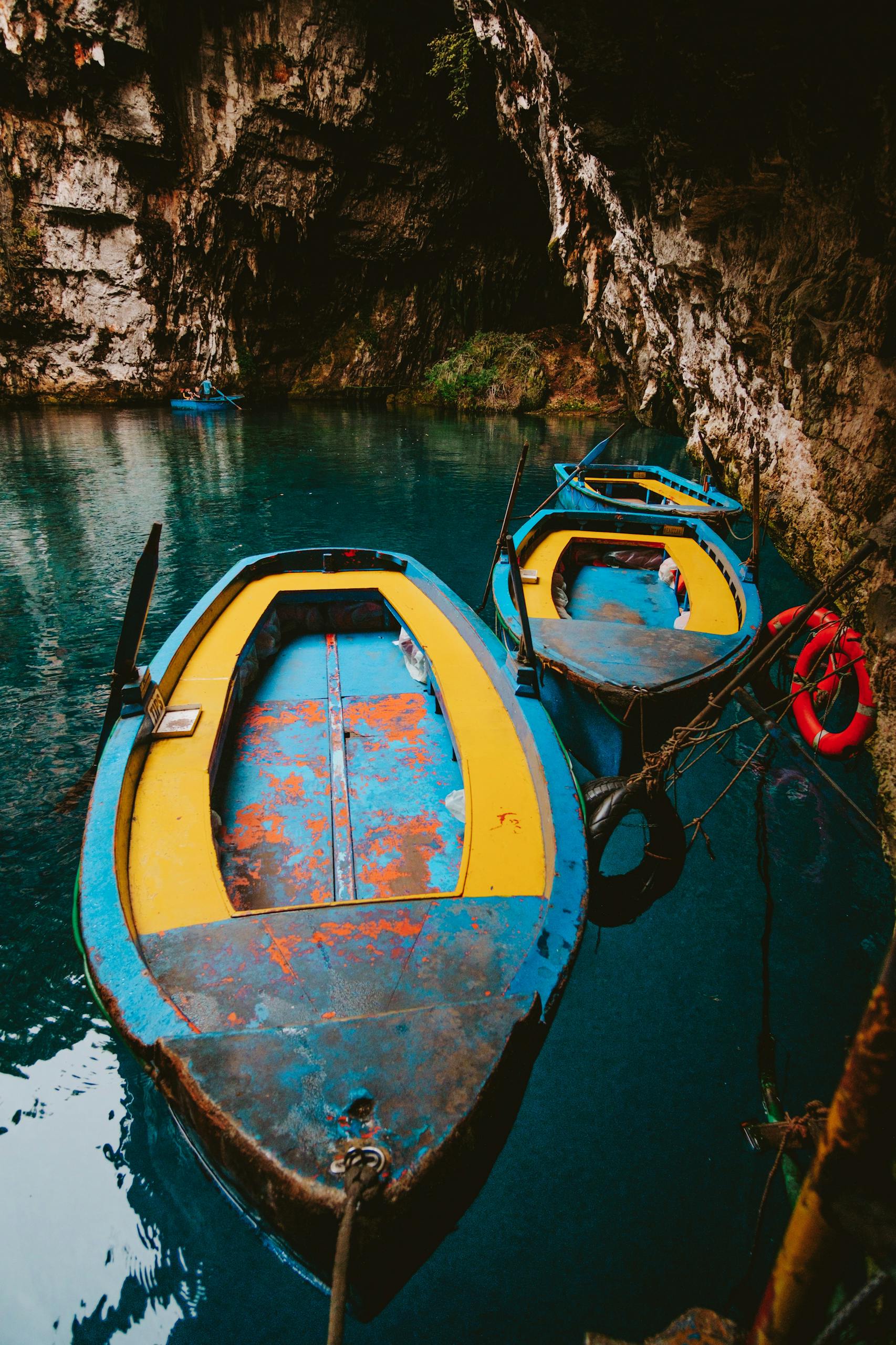 Vibrant yellow and blue boats floating on clear water in Karavomilos cave, Greece.