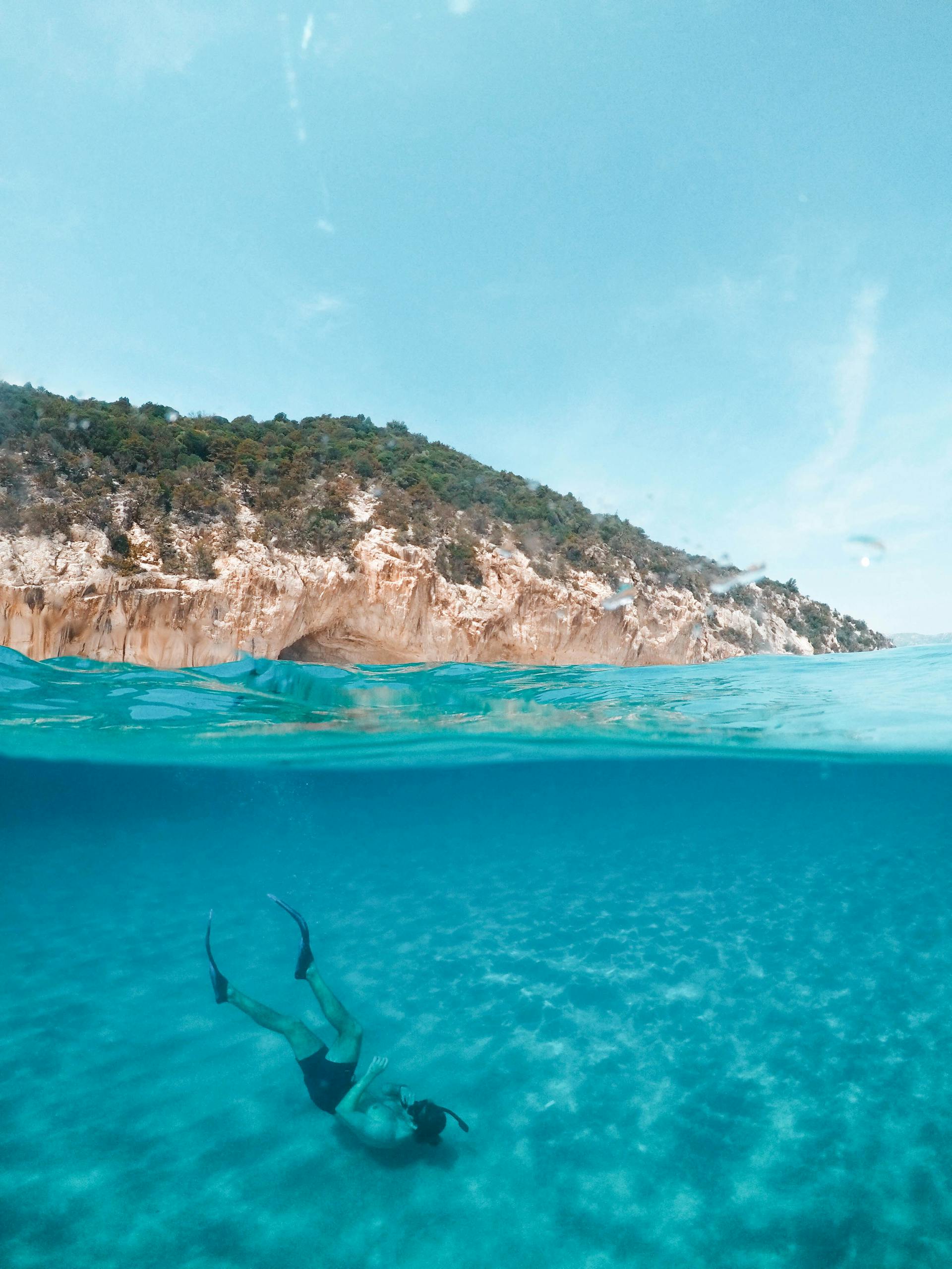 A serene over-under photograph capturing a diver exploring the turquoise waters off the coast of Sardinia, Italy.