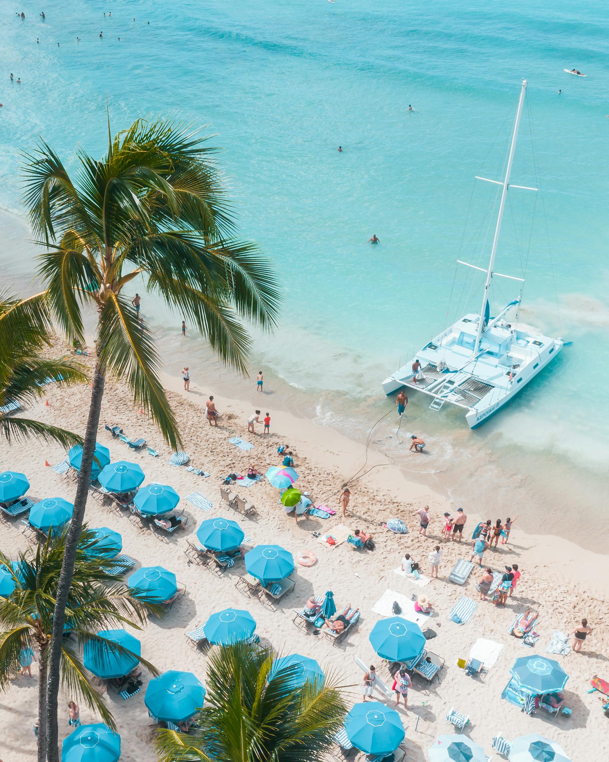 Aerial view of a vibrant Hawaiian beach with turquoise waters and a nearby catamaran.