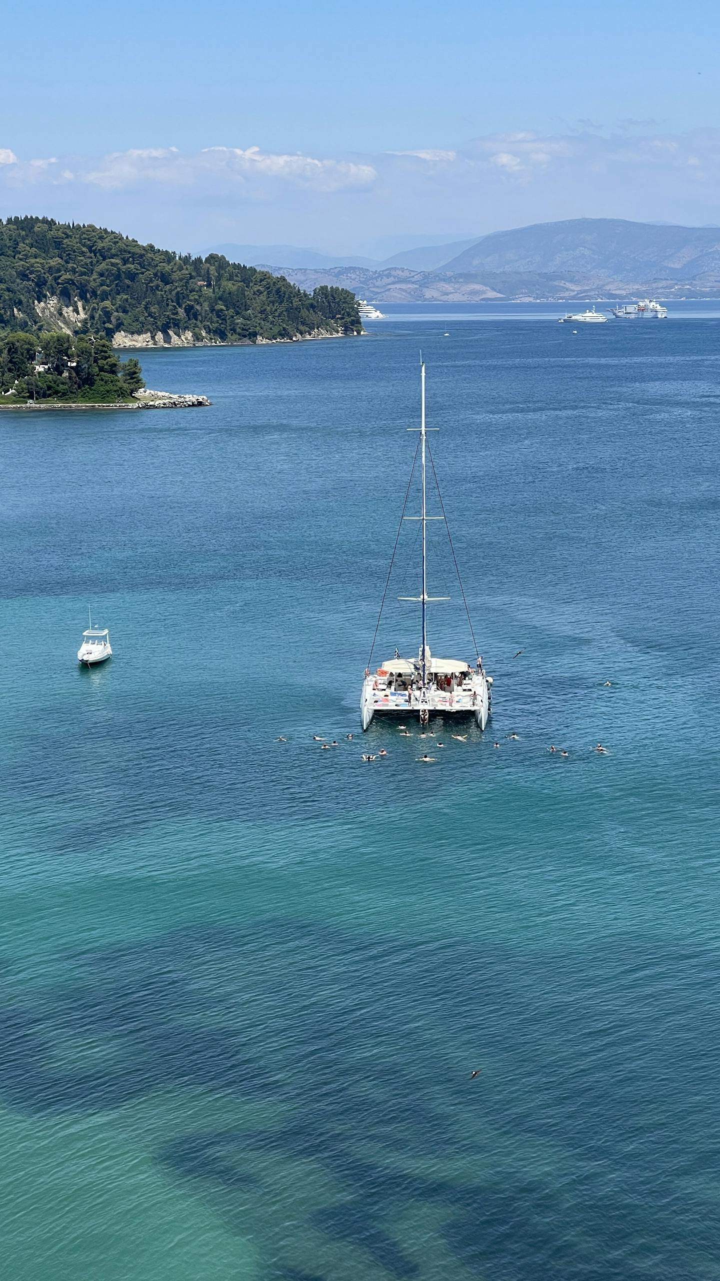 Stunning aerial view of catamaran and motorboat in crystal-clear sea near scenic coastline.